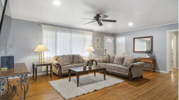 A living room with a wooden floor, two sofas, a coffee table, a ceiling fan, and two lamps.