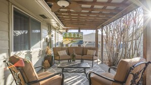 Une terrasse couverte avec un ventilateur de plafond, un coin salon avec des coussins et une table agrémentée d’un vase.