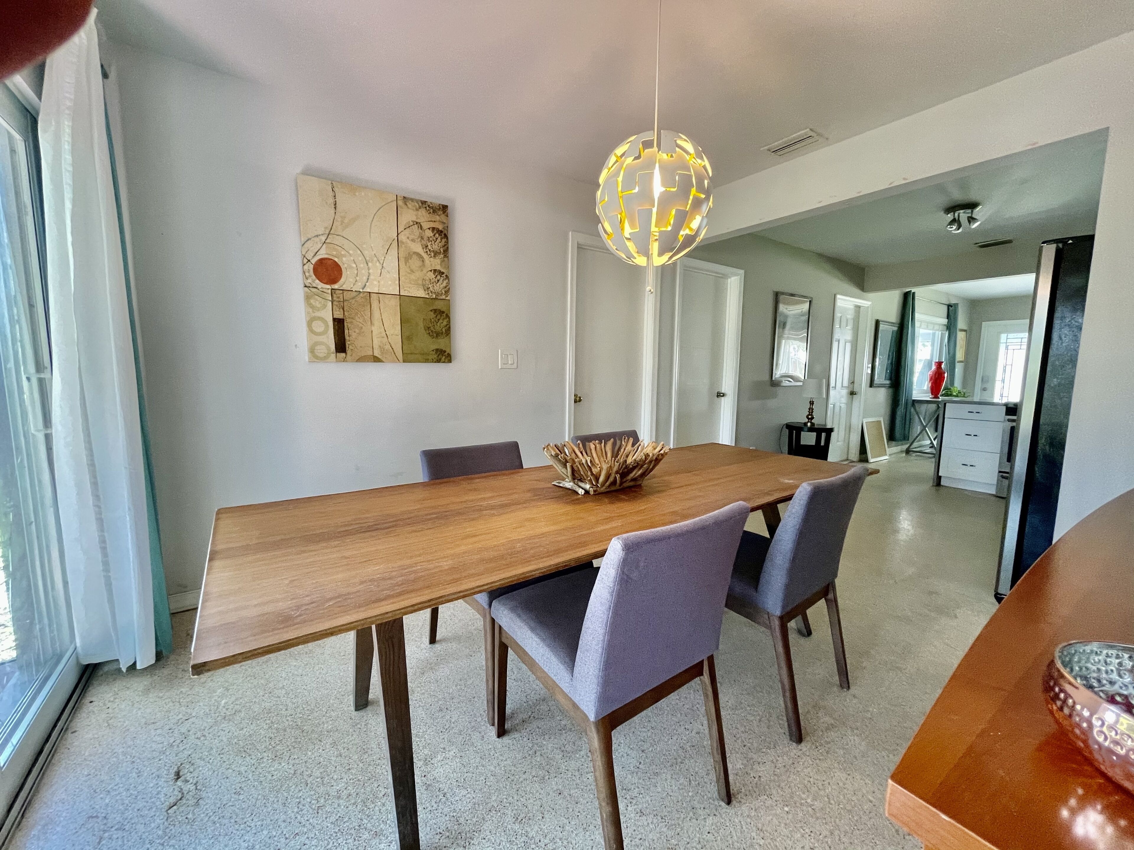 Un comedor moderno con una mesa de madera, sillas tapizadas en gris y una lámpara decorativa tipo globo.
