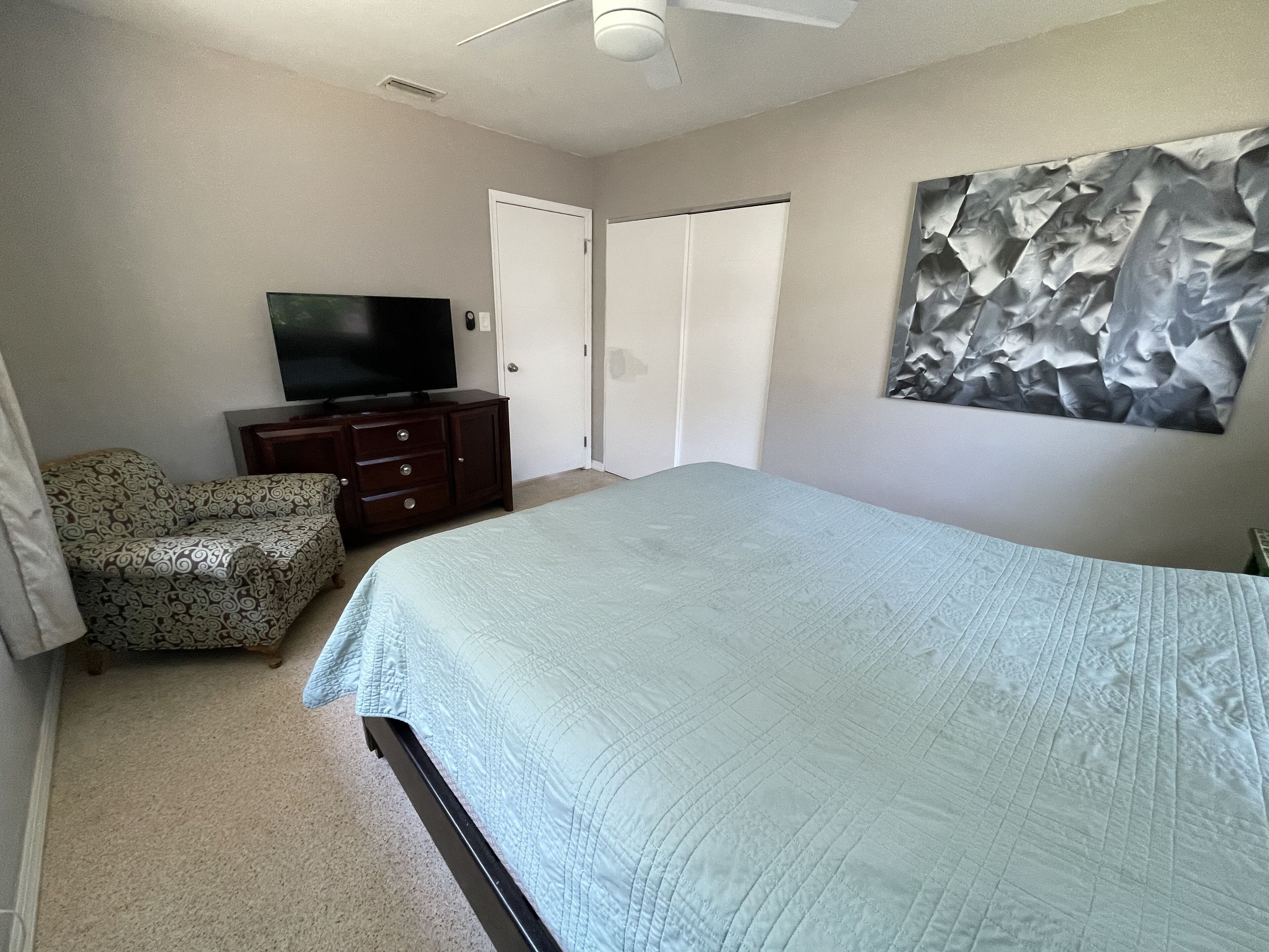 Une chambre à coucher avec un lit, un téléviseur posé sur une commode, une chaise et une porte.