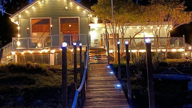 Una terraza de madera que lleva a una casa con luces colgantes y un porche cubierto.