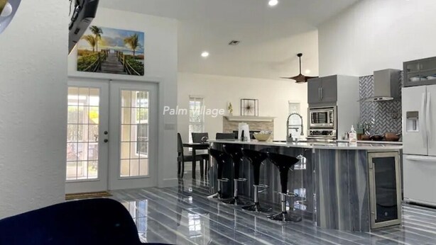 Ett modernt kök med en bänkskiva i marmor, en matplats med barstolar och en utsikt över en palm genom fönstret.