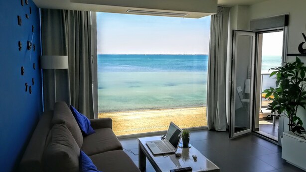 Een moderne woonkamer met een bank, een salontafel en een laptop. Er is een groot raam met uitzicht op de oceaan.