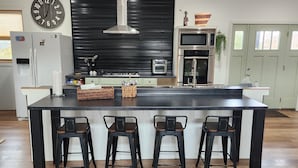 Una cucina moderna con isola centrale, sgabelli da bar, un orologio ed elettrodomestici in acciaio inossidabile.