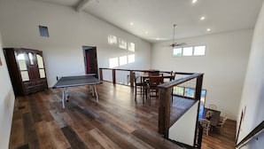 Un'ampia stanza con tavolo da ping pong, pavimento in legno, zona pranzo con sedie e una scala con corrimano.