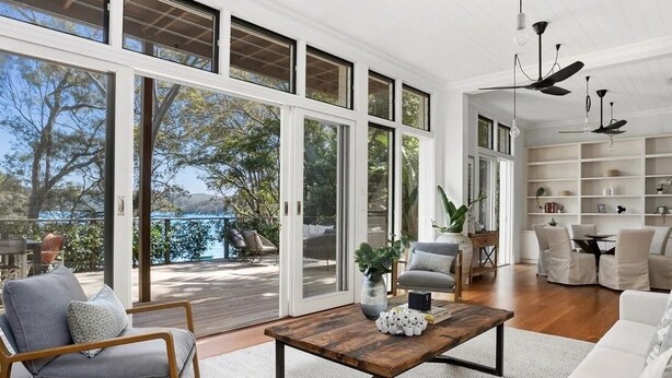 A spacious living area with a large sliding glass door leading to a deck, a wooden coffee table, a grey armchair, and a white sofa.