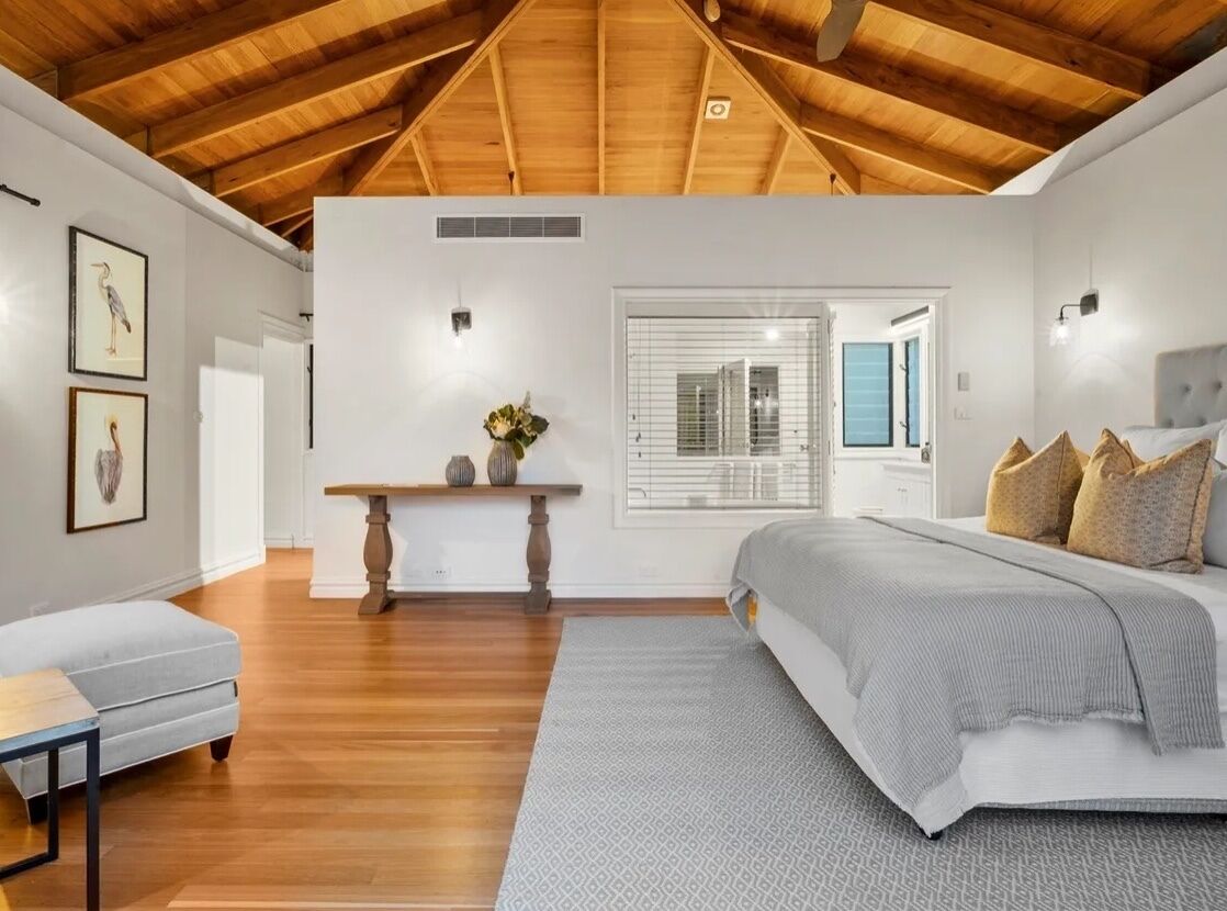 A bedroom with a large bed, a nightstand, a dresser, and a window with blinds.