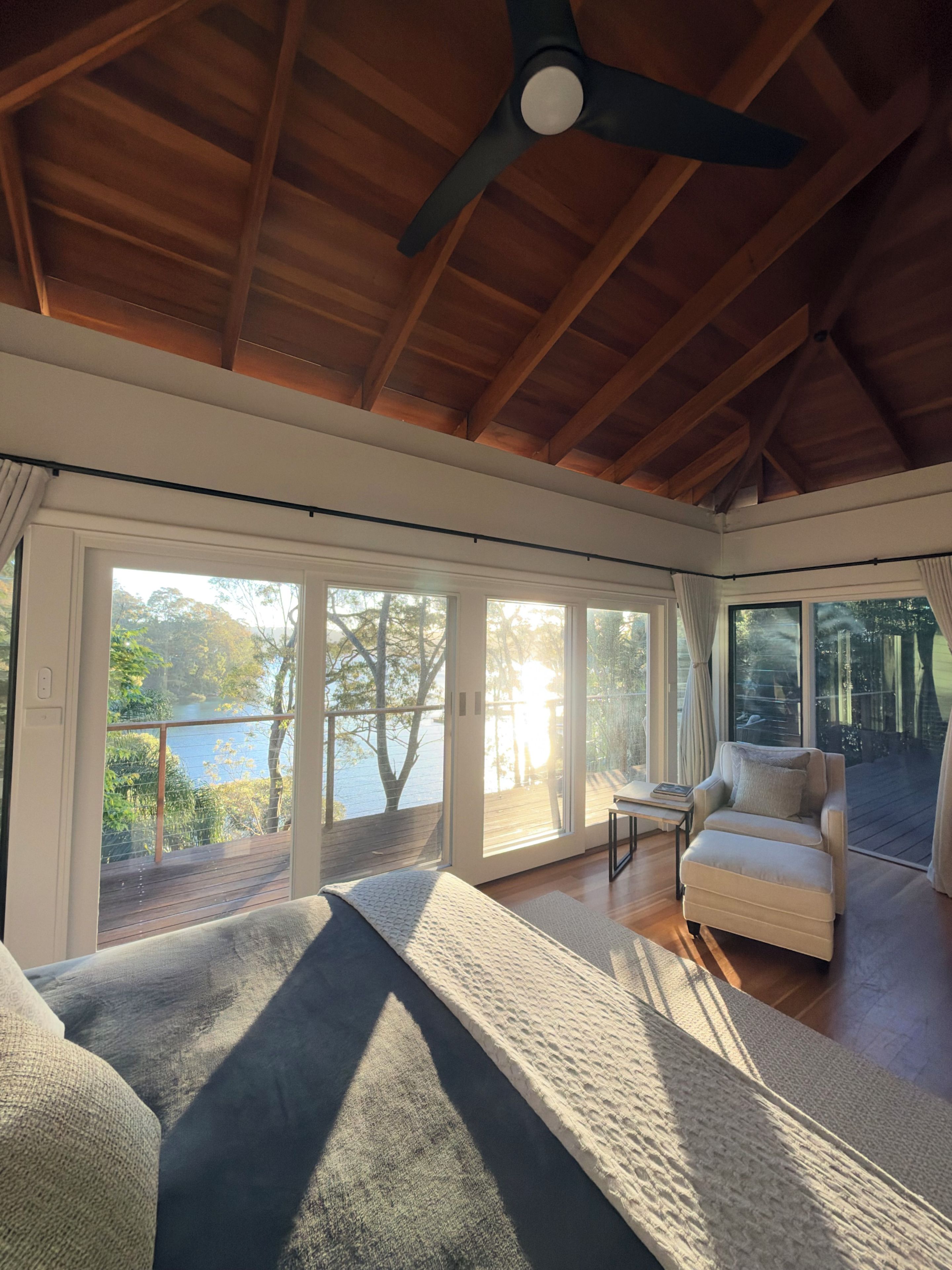 Ein geräumiges Zimmer mit Deckenventilator, großen Schiebeglastüren, die auf eine Terrasse führen, und einer gemütlichen Sitzecke mit Sofa und Sessel.