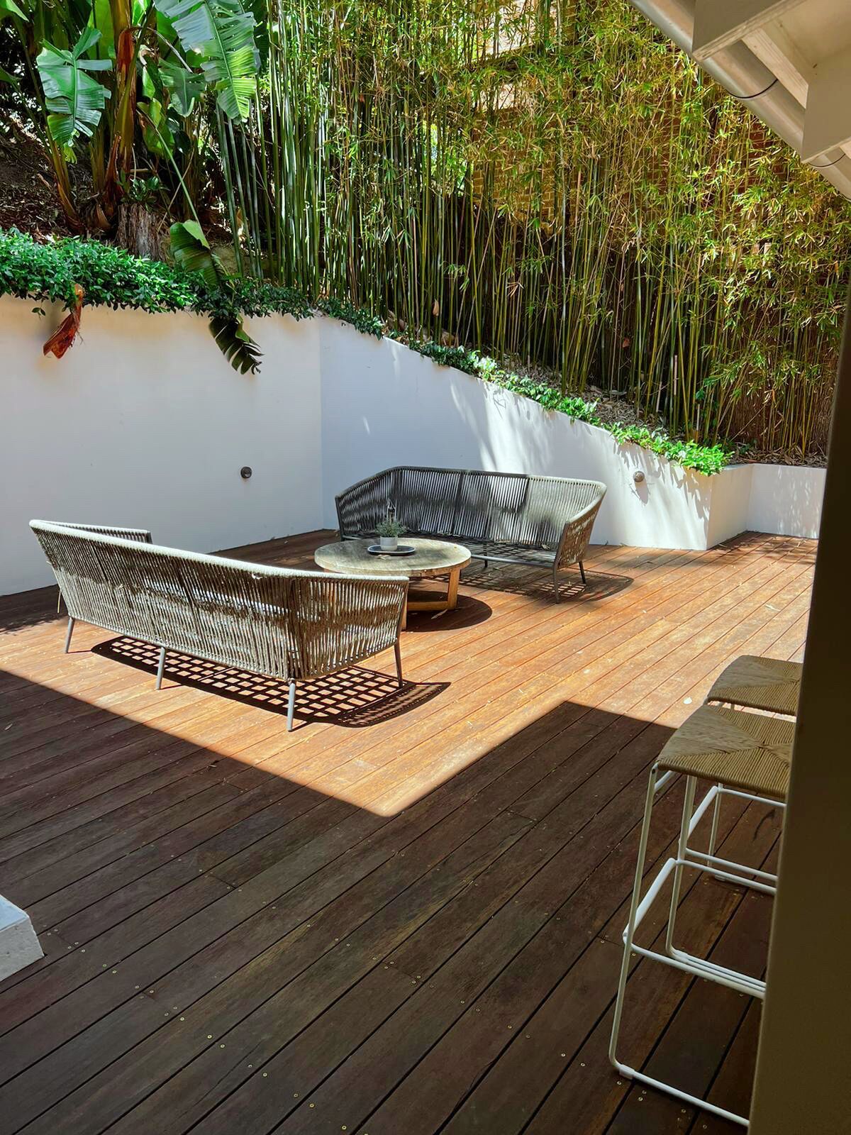 A wooden deck with wicker furniture, a white wall, and bamboo plants.