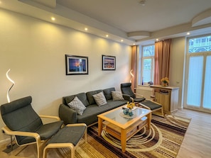 Uma sala de estar moderna com um sofá, duas poltronas, uma mesa de centro de vidro e um tapete estampado.