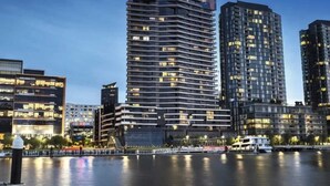 A waterfront cityscape with modern high-rise buildings, a river, and a boat docked at the pier.