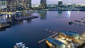 A waterfront hotel with a modern design, featuring a dock with boats, a marina, and a city skyline in the background.