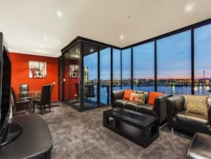 Enjoy a panoramic view of the city and water from this stylish living room, featuring a comfortable sofa, coffee table, and flat-screen TV.