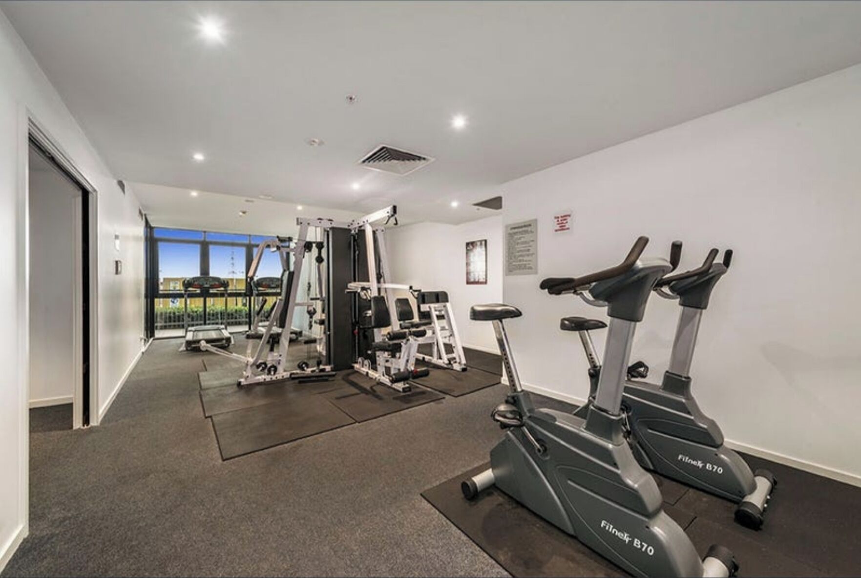 A gym with cardio machines, weightlifting equipment, and a large window offering a view.