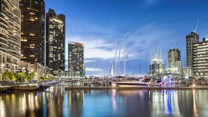A waterfront marina with modern buildings, including a distinctive curved structure and a tall skyscraper with a unique roof design.