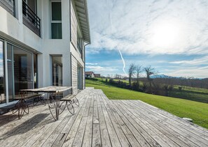 Een modern huis met een houten terras en een glazen deur die uitkomt op een patio.