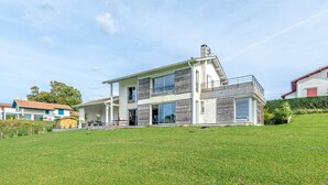 Une maison moderne à deux étages, dotée d’un toit plat, de grandes fenêtres et d’un patio couvert.