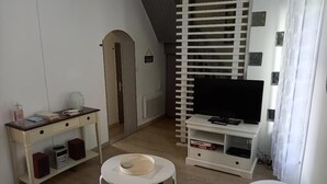 A compact living space with a TV, a small dining table, a white sofa, and a bookshelf.