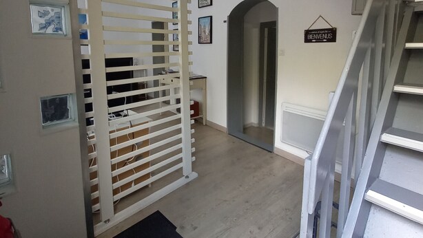 A staircase leading to a landing with a black mat, a white partition with horizontal slats, and a 'BIENVENUS' sign on the wall.