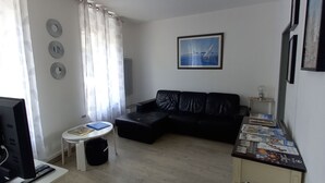 A living room with a black leather sofa, a small white table, and a TV on a stand.