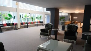 Un amplio vestíbulo con zonas de estar, mostrador de recepción y ventanas grandes con plantas.