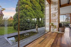 Ein modernes Interieur mit einer Steinwand, Holzböden, einem kleinen Teich und Blick auf einen üppigen Garten.
