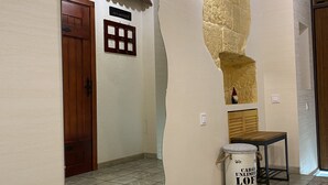 Un pasillo con puerta de madera, una lámpara en la pared, una pequeña mesa y un adorno mural.