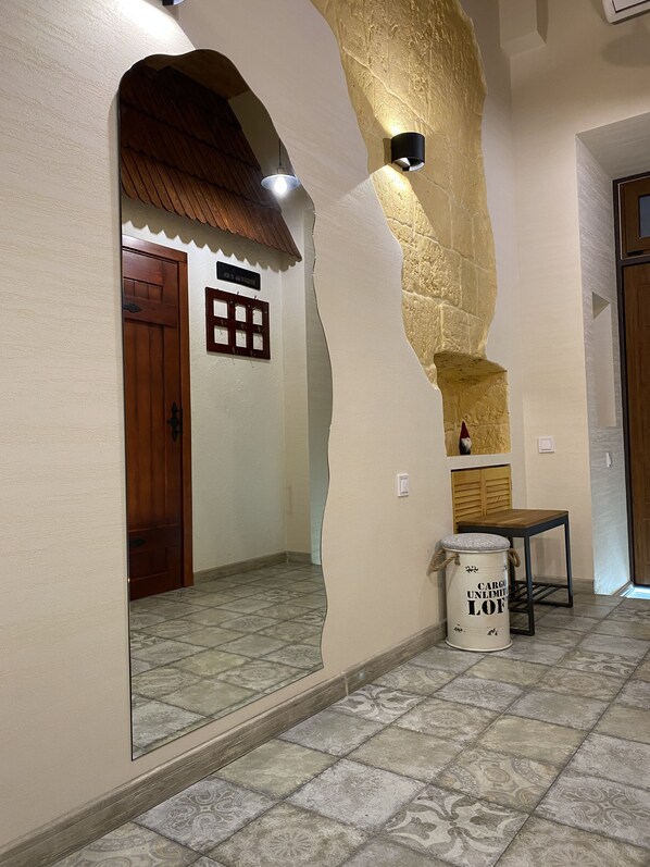 Un couloir avec une porte en bois, un luminaire fixé au mur, une petite table et un élément décoratif mural.