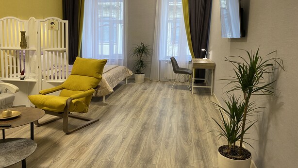 Una sala de estar moderna con un sillón amarillo, una mesa de centro de madera, una mesita auxiliar, una planta en maceta, un escritorio con una lámpara y un televisor montado en la pared.