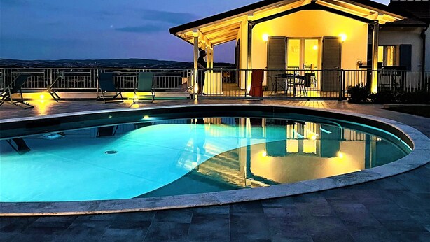 A swimming pool with a covered patio area, a view of the surrounding landscape, and a building with a balcony. - Luxury villa, swimming pool, shaded terraces, panoramic view, sauna fitness room (CAMPAGNATICO (GR))