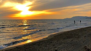 A beach with two people walking along the shore during sunset. - Luxury villa, swimming pool, shaded terraces, panoramic view, sauna fitness room (CAMPAGNATICO (GR))