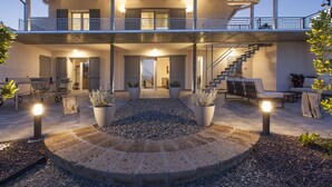 A two-story house with a covered patio, outdoor seating, and a staircase leading to the upper level. - Luxury villa, swimming pool, shaded terraces, panoramic view, sauna fitness room (CAMPAGNATICO (GR))