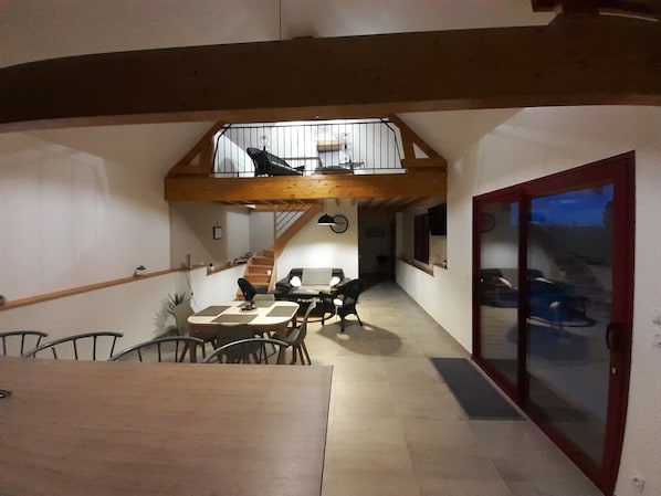 A dining area with a wooden table and chairs, a staircase leading to an upper level, and a sliding glass door to the right. - Gîte Normand Le Danay 4* between Etretat and Le Havre (saint Jouin Bruneval)