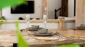 Rustiikkinen puinen pöytä, jonka päällä on sinisiä keramiakulhoja ja viinilaseja. Pöytä on sijoitettu huoneeseen, jossa on puinen kaappi ja seinälle asennettu televisio.