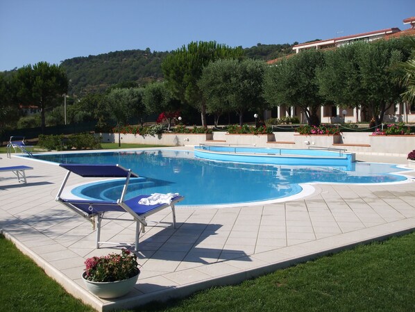 A swimming pool with lounge chairs and a view of a hill with trees and a building in the background. - Giorgia's House in Capo Vaticano, Apartment with Wi-Fi, Air Conditioning, and a Pool (Santa Maria di Ricadi)