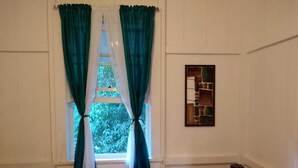 A room with a bed, a window with green curtains, a small wooden dresser, and a wall-mounted shelf with a mirror. - Remodeled house in Gamboa. Next to the Panama Canal, nature and tranquility. (Gamboa)