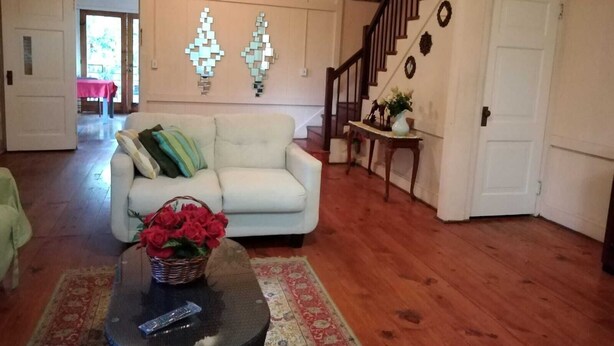A living room with a white sofa, a coffee table with a basket of red flowers, a wooden staircase, and a door with a wreath. - Remodeled house in Gamboa. Next to the Panama Canal, nature and tranquility. (Gamboa)