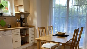 Eine Küche mit Holztisch und Stühlen, einer Kaffeemaschine und einem Fenster mit Vorhängen.