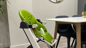 Une chambre moderne avec une poussette pour bébé aux couleurs vert et blanc, un miroir rond et une table à manger avec des chaises.