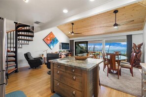 A modern kitchen with a wooden ceiling, a dining area with a view, and a spiral staircase.
