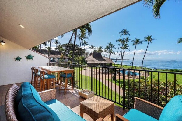 A balcony with a view of the ocean, a pool, and palm trees.