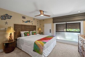 A bedroom with a bed, nightstands, a ceiling fan, decorative wall art, and a view through a window.