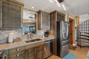 A kitchen with a stone backsplash, wooden cabinets, stainless steel appliances, and a view through the window.