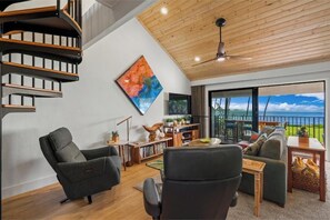 A modern living room with a spiral staircase, a large painting, a TV, and a view of the ocean.