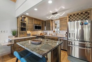 A modern kitchen with wooden cabinets, a stainless steel refrigerator, granite countertops, and a built-in island with seating.