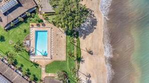 An aerial view of a beachfront property with a swimming pool, palm trees, and a beach.