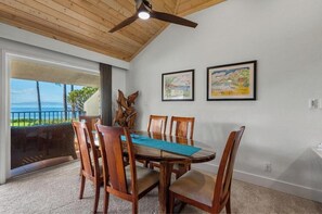 A dining area with a wooden table and chairs, a ceiling fan, and two framed artworks on the wall. - Ma'alaea Surf #C-7 – Oceanfront Getaway with Spectacular Views & Pool (Kihei, Maui)