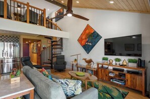 A spacious living area with a staircase, a flat-screen TV, and a bookshelf.