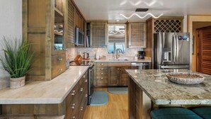 A modern kitchen with wooden cabinets, a granite countertop, a built-in oven, and a stainless steel refrigerator. - Ma'alaea Surf #C-7 – Oceanfront Getaway with Spectacular Views & Pool (Kihei, Maui)