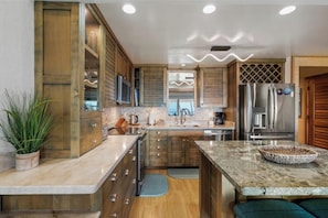 A modern kitchen with wooden cabinets, a granite countertop, a built-in oven, and a stainless steel refrigerator.